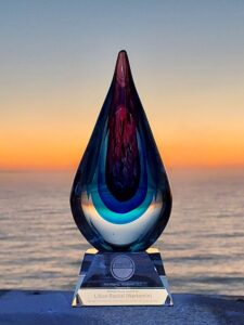 MAVO Muse award a crystal teardrop shape with concentric colours from clear through blues to red at the top is pictured against a Virginia coastline sunset